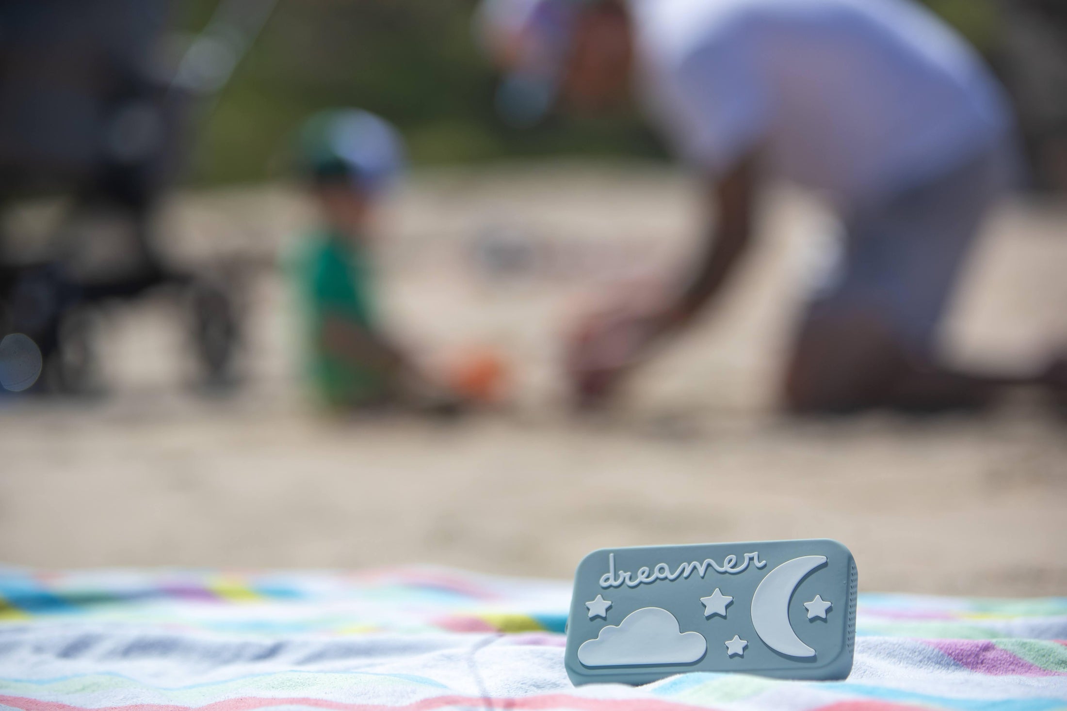 Dreamer baby sound machine on a beach towel as family plays in the background (Sage-Dreamer)